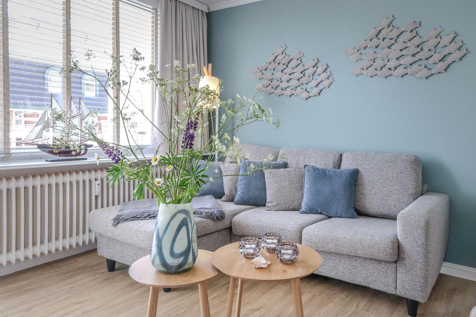 Ein Wohnzimmer mit grauem Sofa, Holztischen und Wanddekoration aus Fischen.