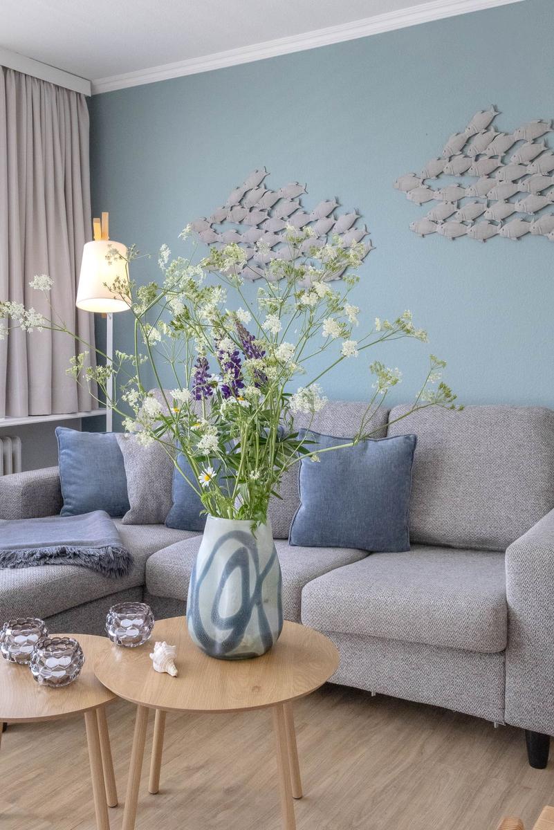 Ein Wohnzimmer mit grauem Sofa, Blumenvase und Wanddekoration.
