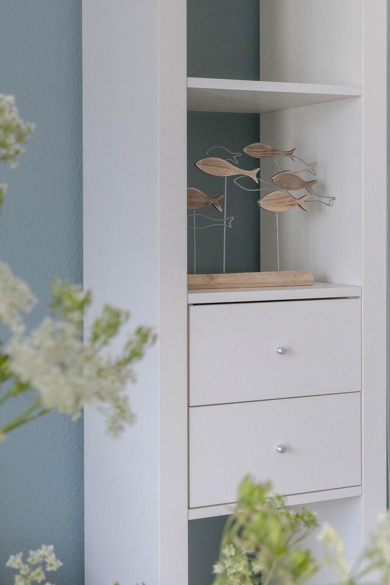 Weißer Schrank mit zwei Schubladen und einer Ablagefläche mit Holzfischen.