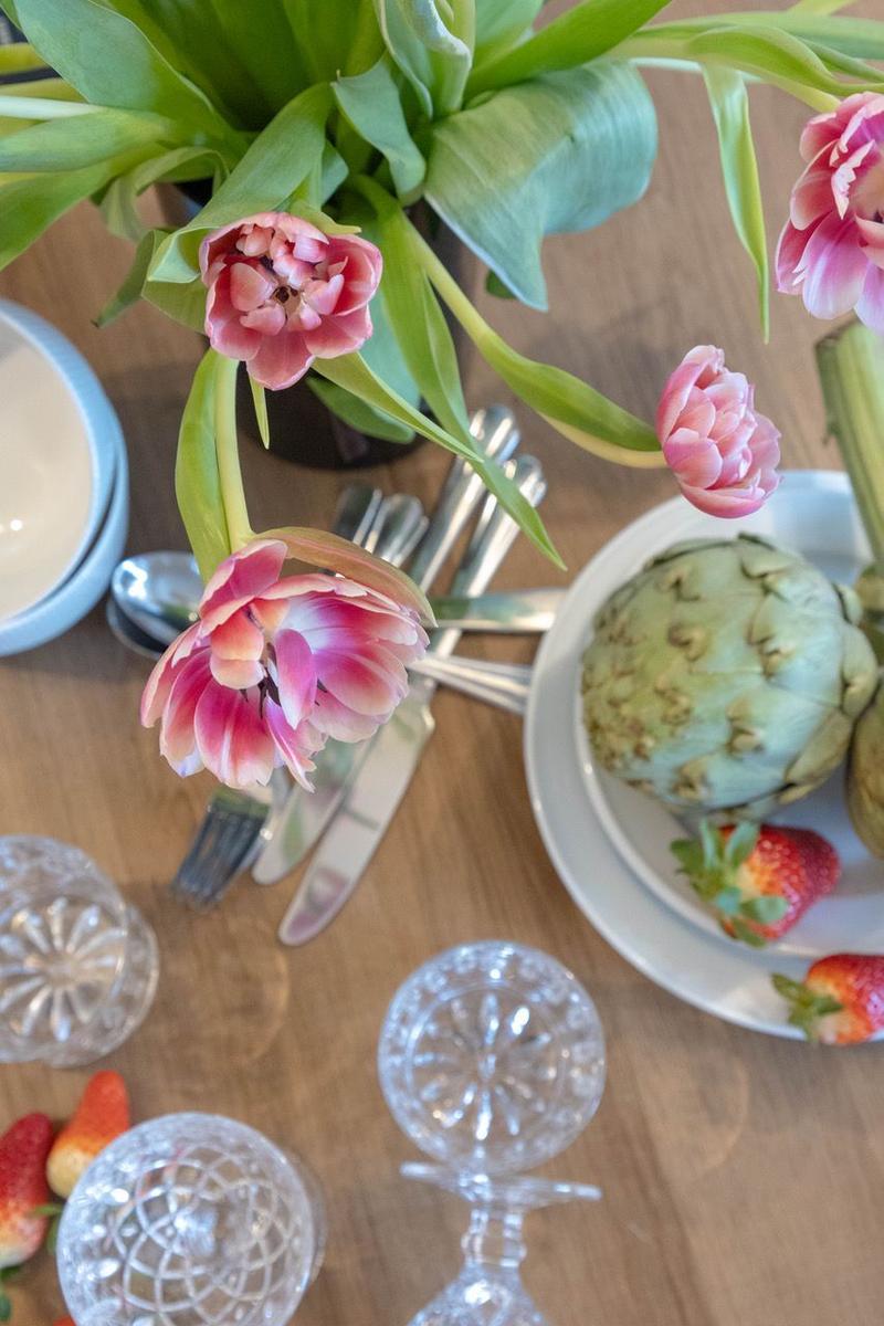 Tisch mit Tulpen, Artischocken und Erdbeeren sowie Gläser und Besteck.