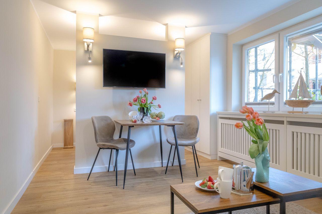 Essbereich mit Tisch, zwei Stühlen und Fernseher an der Wand. Fenster mit Blick nach draußen.
