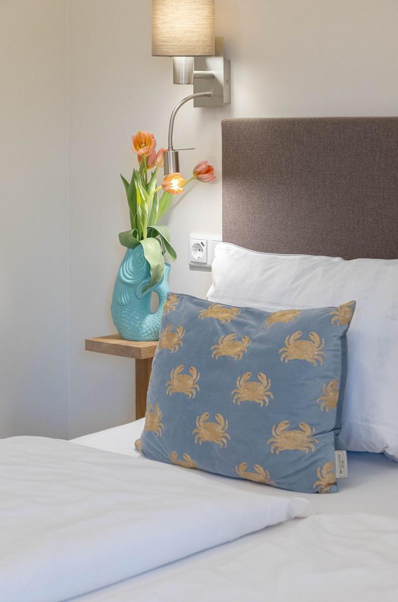 Schlafzimmer mit Bett, Kissen und Nachttisch mit Vase und Blumen.