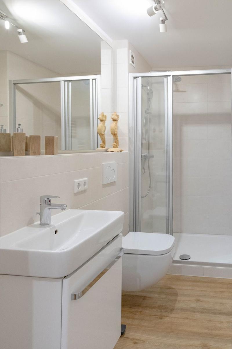 Badezimmer mit Dusche, Waschbecken und Toilette. Holzdielen und Spiegel mit Dekoration.