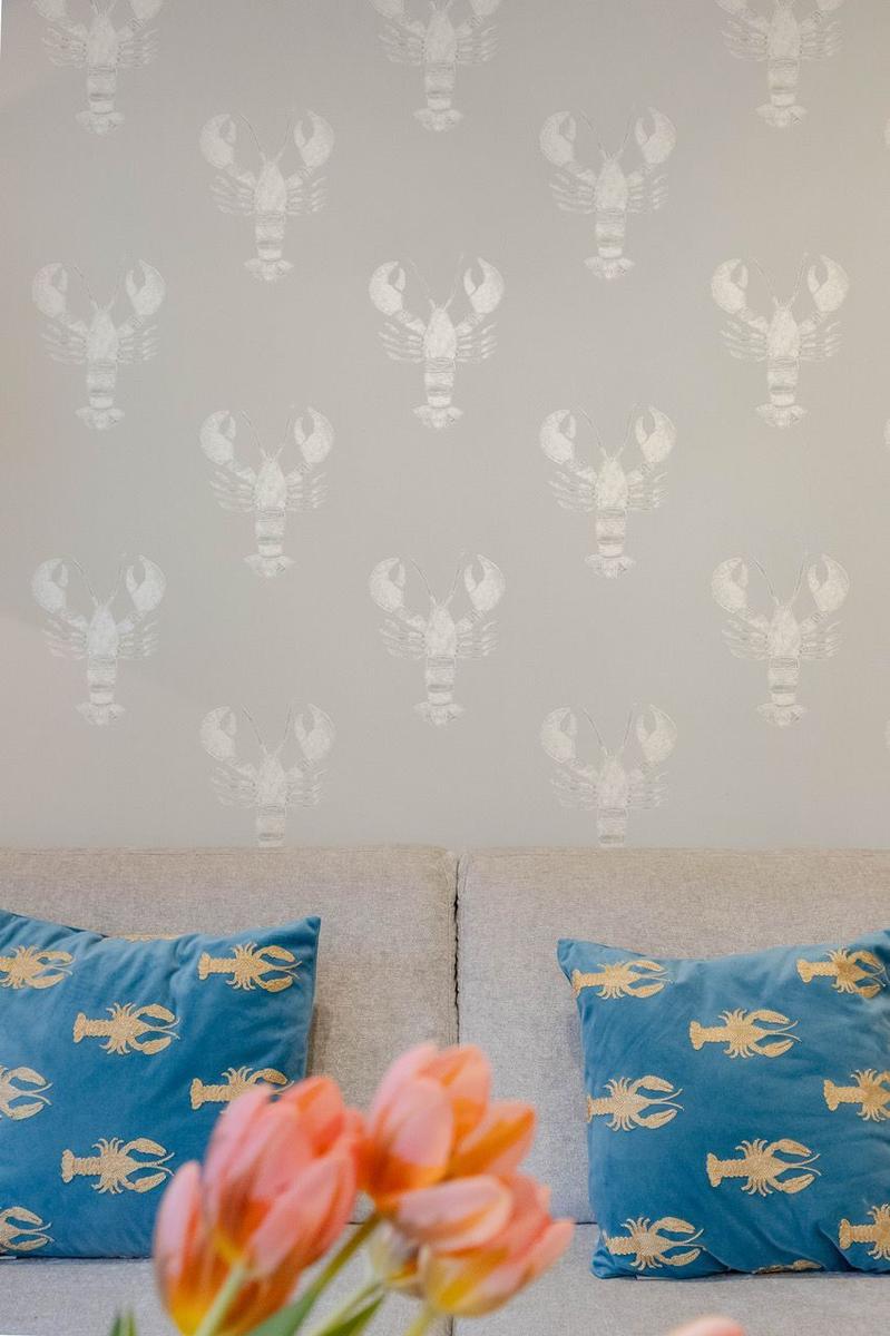 Wand mit Hummer-Motiv, grauer Sofa mit blauen Kissen und Tulpen im Vordergrund.