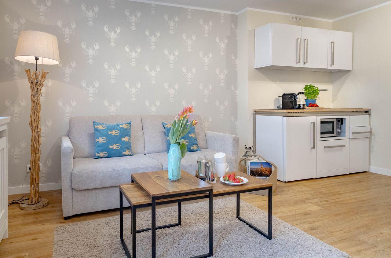 Wohnbereich mit Sofa, Tisch und Küchenzeile mit Mikrowelle.