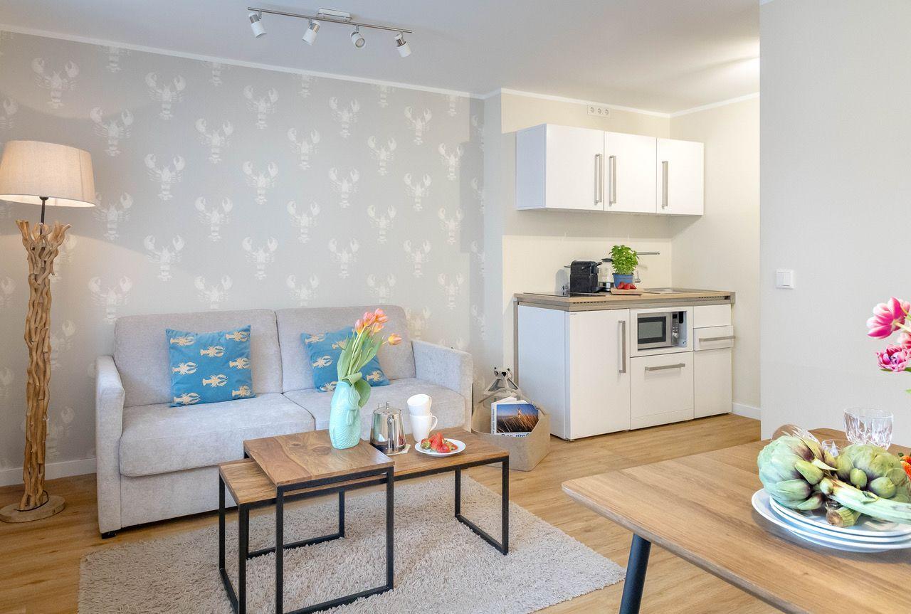 Wohnbereich mit Sofa, Tisch und Küchenzeile. Wand mit Krebsmotivtapete.