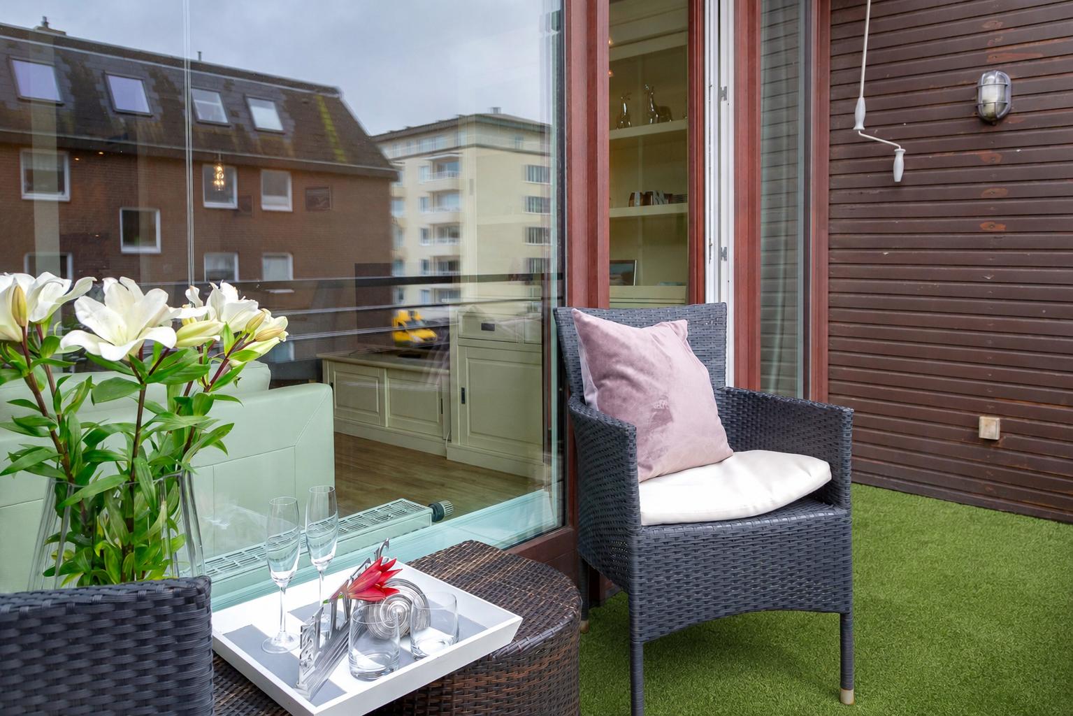 Terrasse mit Stuhl, Tisch und Blumen. Blick in Wohnzimmer durch Glastür.