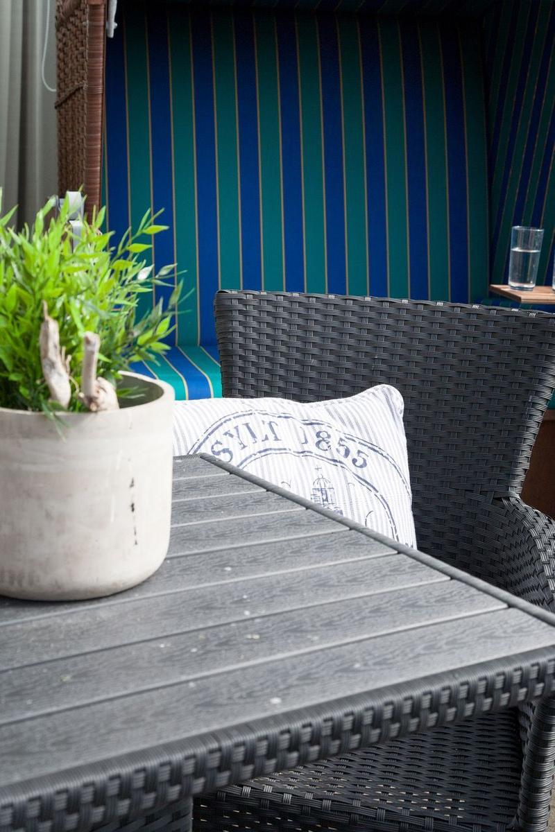 Terrassentisch mit Stuhl, Pflanze und Kissen mit Aufdruck.