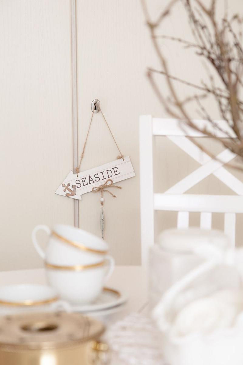 Ein Schild mit der Aufschrift SEASIDE hängt an einer Wand neben einem weißen Stuhl.