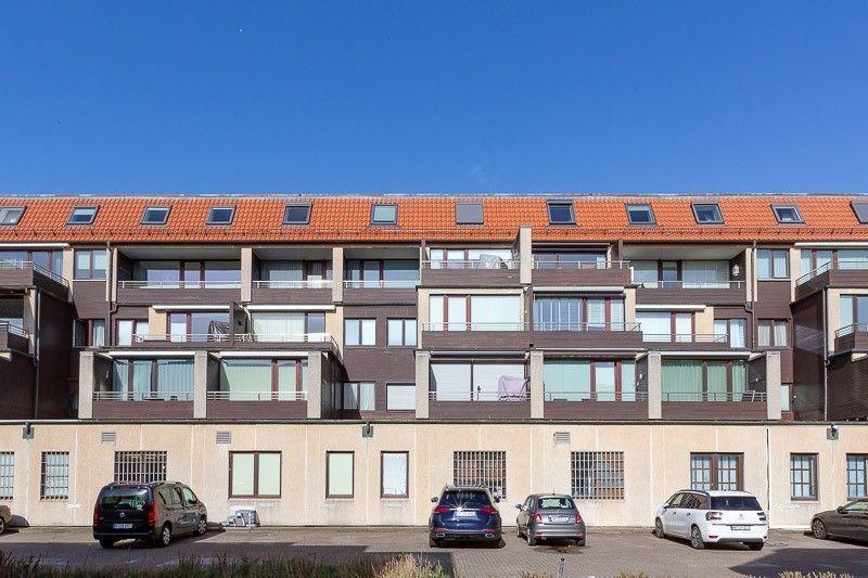 Modernes Mehrfamilienhaus mit Balkonen und rotem Dach unter blauem Himmel.