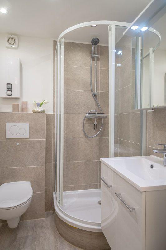 Badezimmer mit Dusche, Waschbecken und Toilette. Fliesenwand und Holzboden.