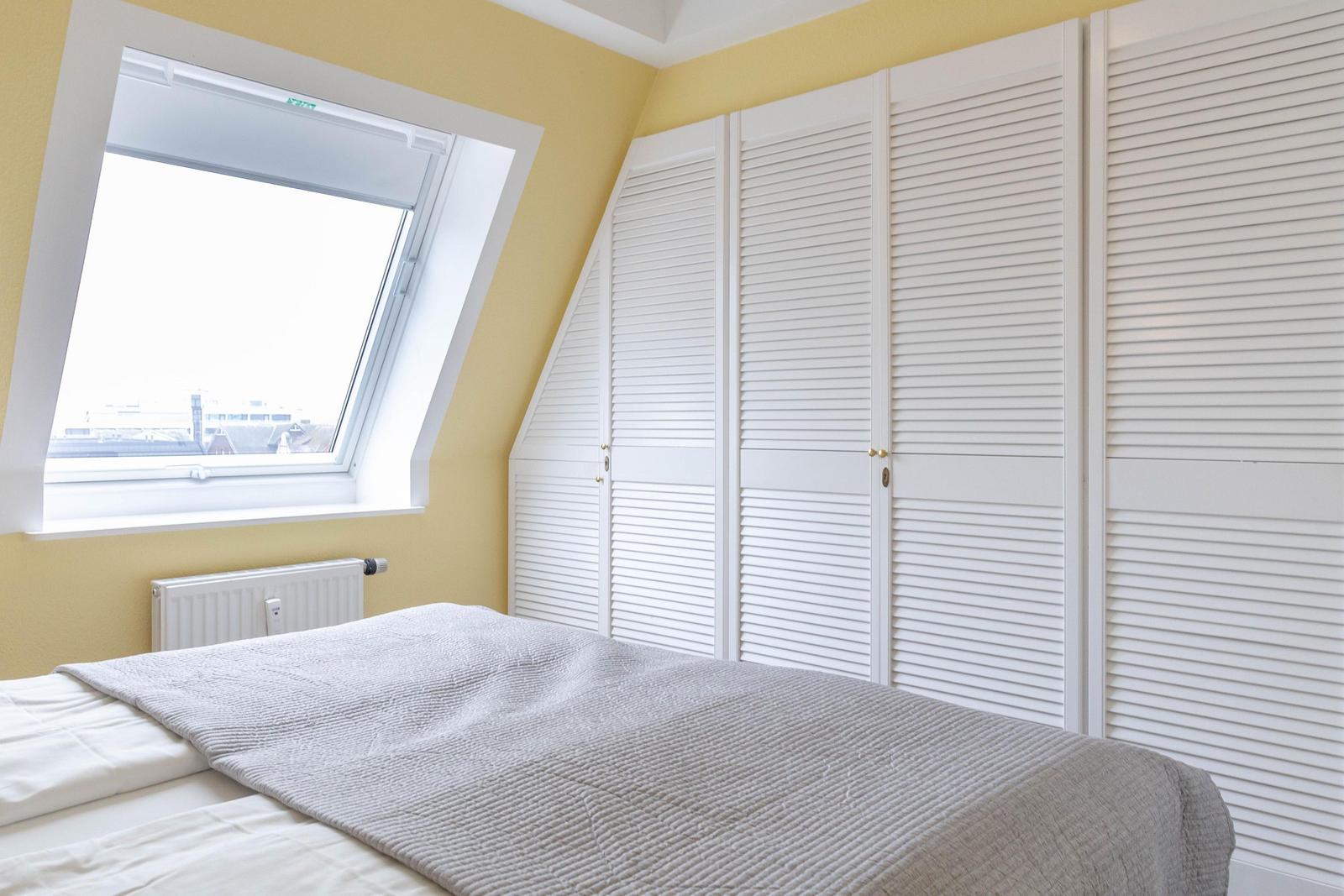Schlafzimmer mit Dachfenster, weißer Schrankwand und Bett mit grauer Bettdecke.
