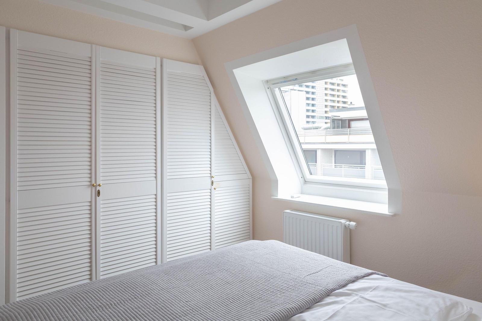 Schlafzimmer mit Dachschrägen, Dachfenster und weißem Schrank.