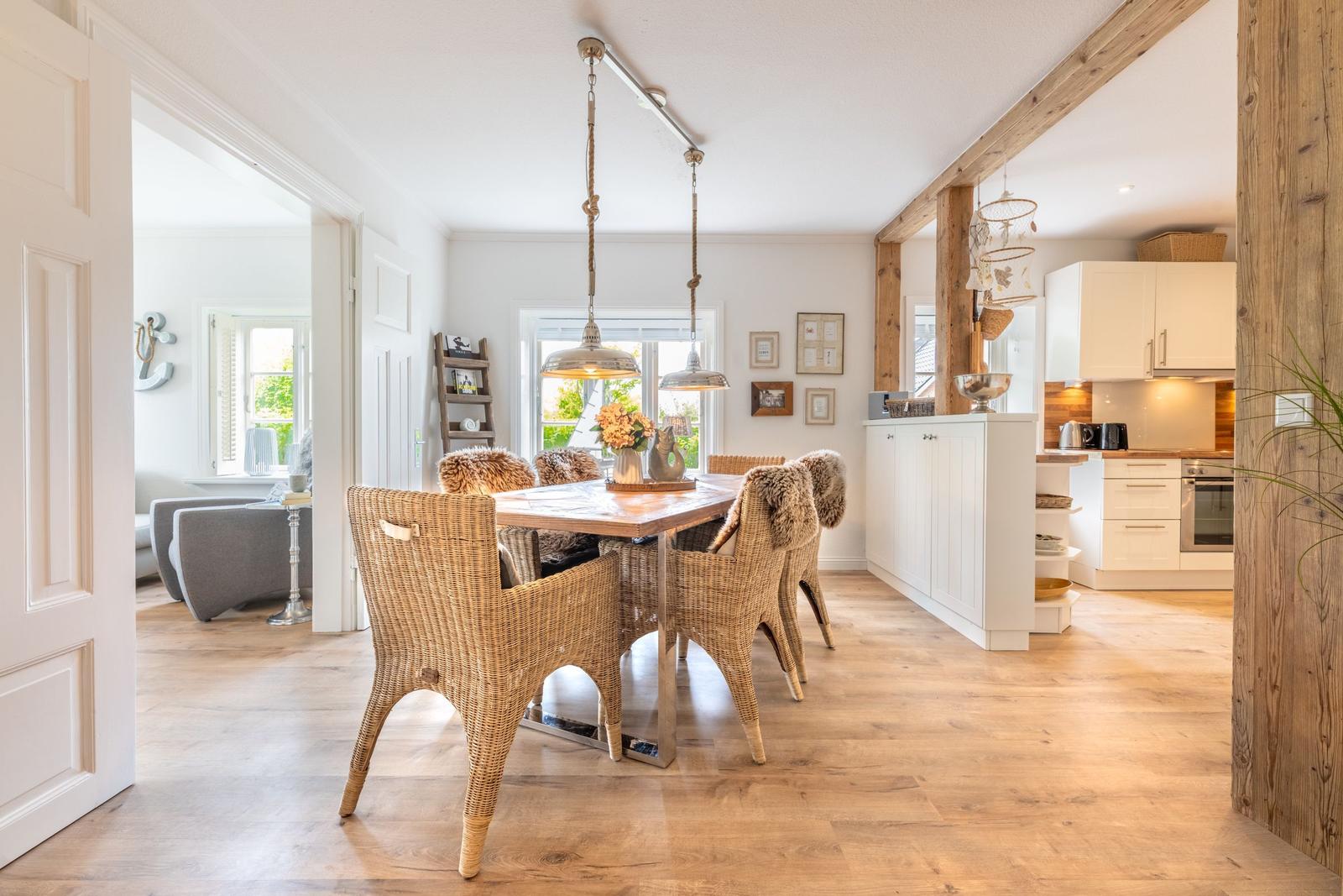 Essbereich mit Holztisch, Rattanstühlen und Küchenbereich im Hintergrund.
