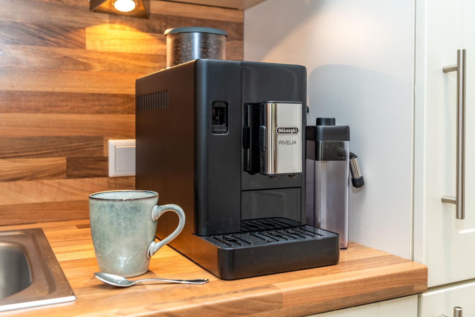Espresso-Kaffeemaschine auf Küchenarbeitsfläche mit Tasse und Löffel.