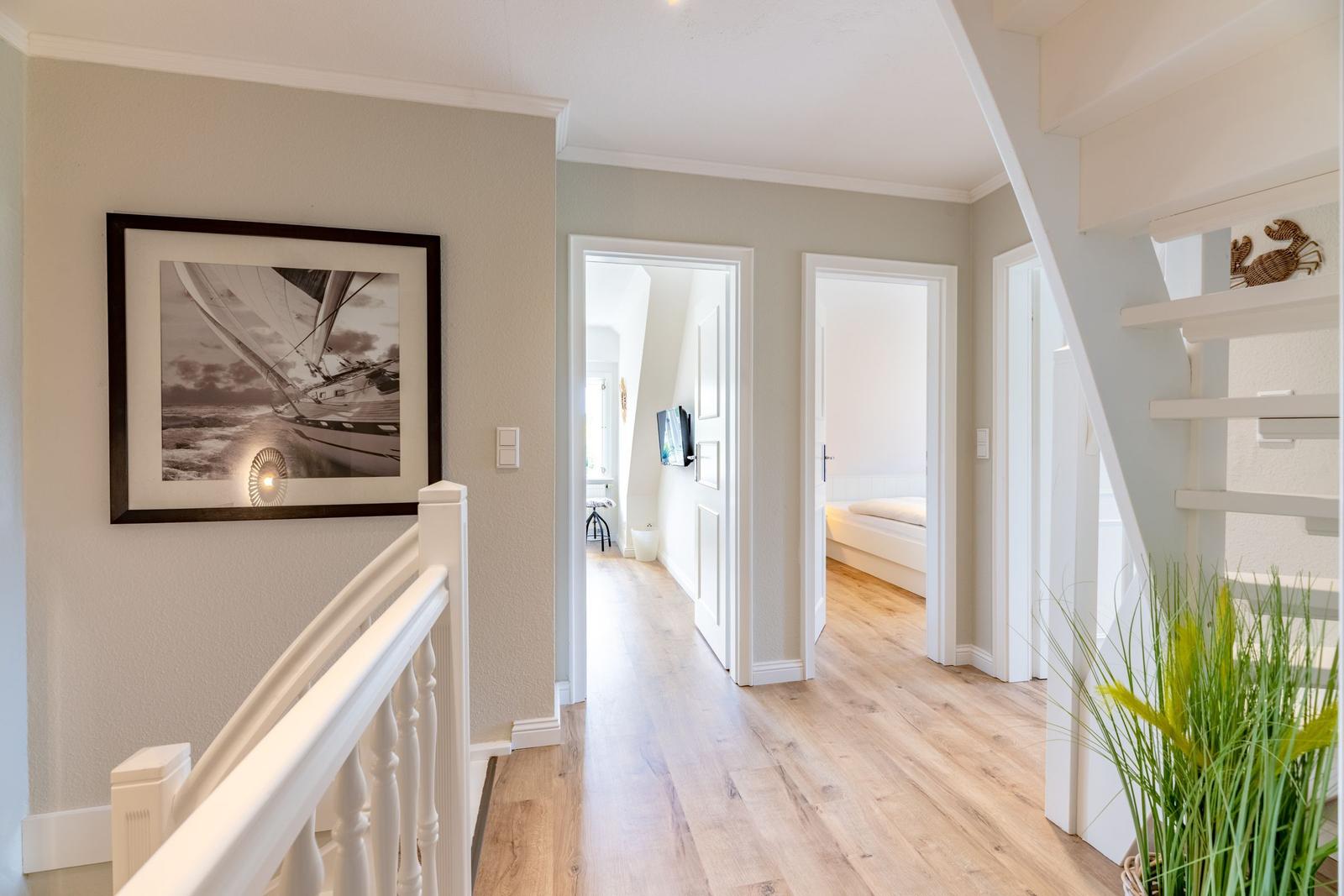 Hausgang mit Holzboden, Treppe und Bild an der Wand. Blick in Wohn- und Schlafzimmer.