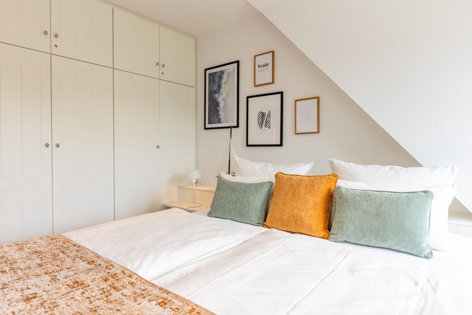 Schlafzimmer mit Dachschrägen, weißem Bett und farbigen Kissen.