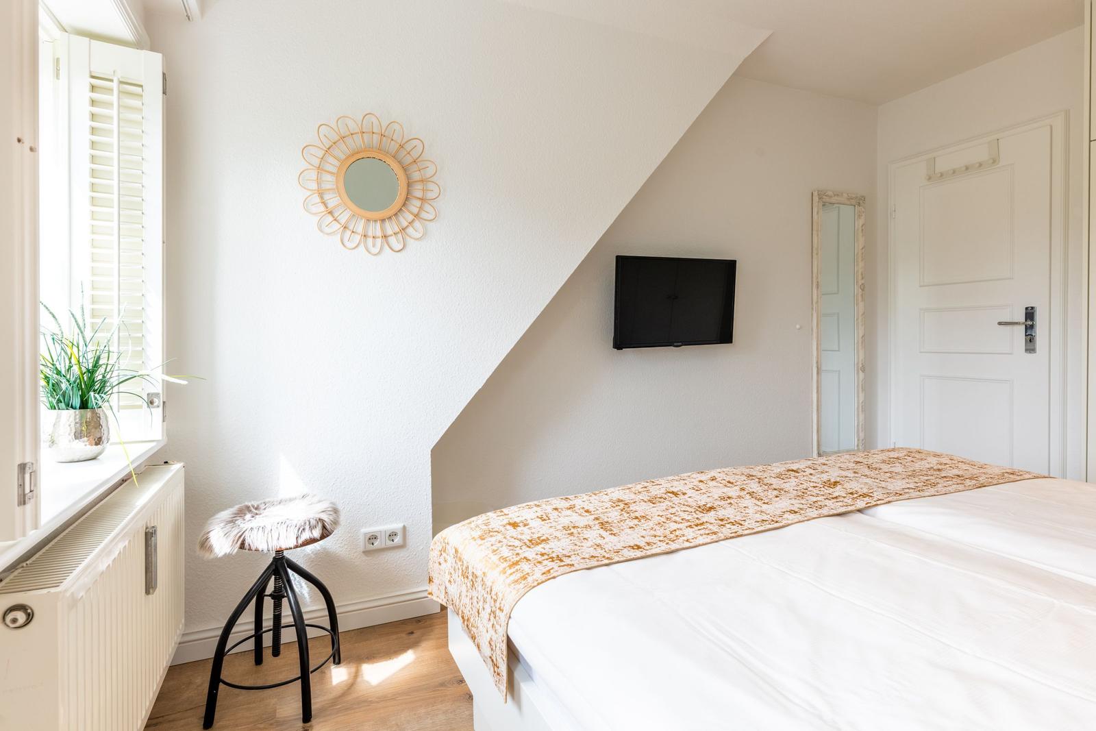 Schlafzimmer mit Bett, Fernseher und Fenster mit Pflanze.