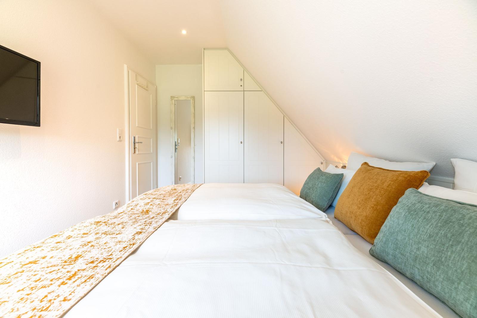 Schlafzimmer mit Doppelbett, Kleiderschrank und Wandfernseher unter Dachschrägen.