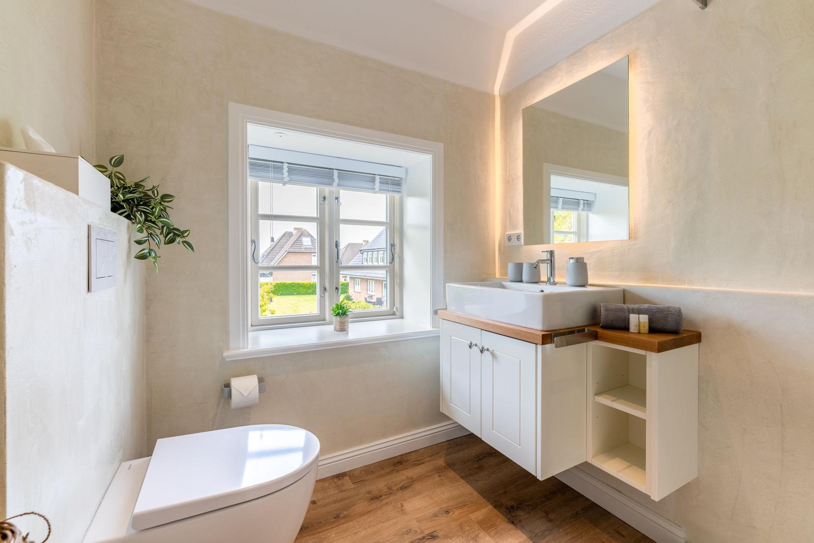 Badezimmer mit Waschtisch, Spiegel und Toilette. Fenster mit Blick auf Garten.