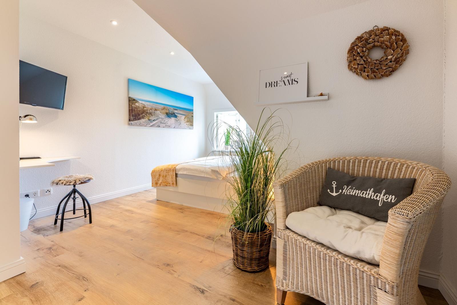 Schlafzimmer mit Bett, Wicker-Sofa, Pflanze und Wandbild. TV und Schreibtisch im Raum.