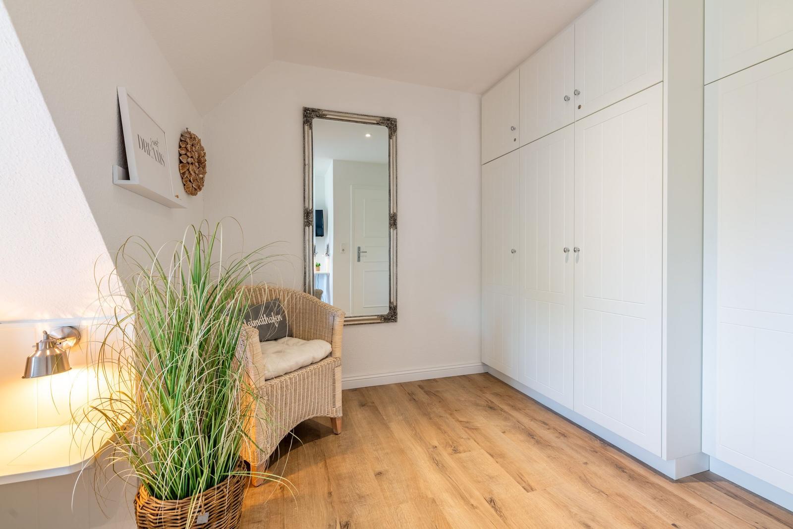 Schlafzimmer mit weißen Schränken, Holzboden und Sitzgelegenheit.