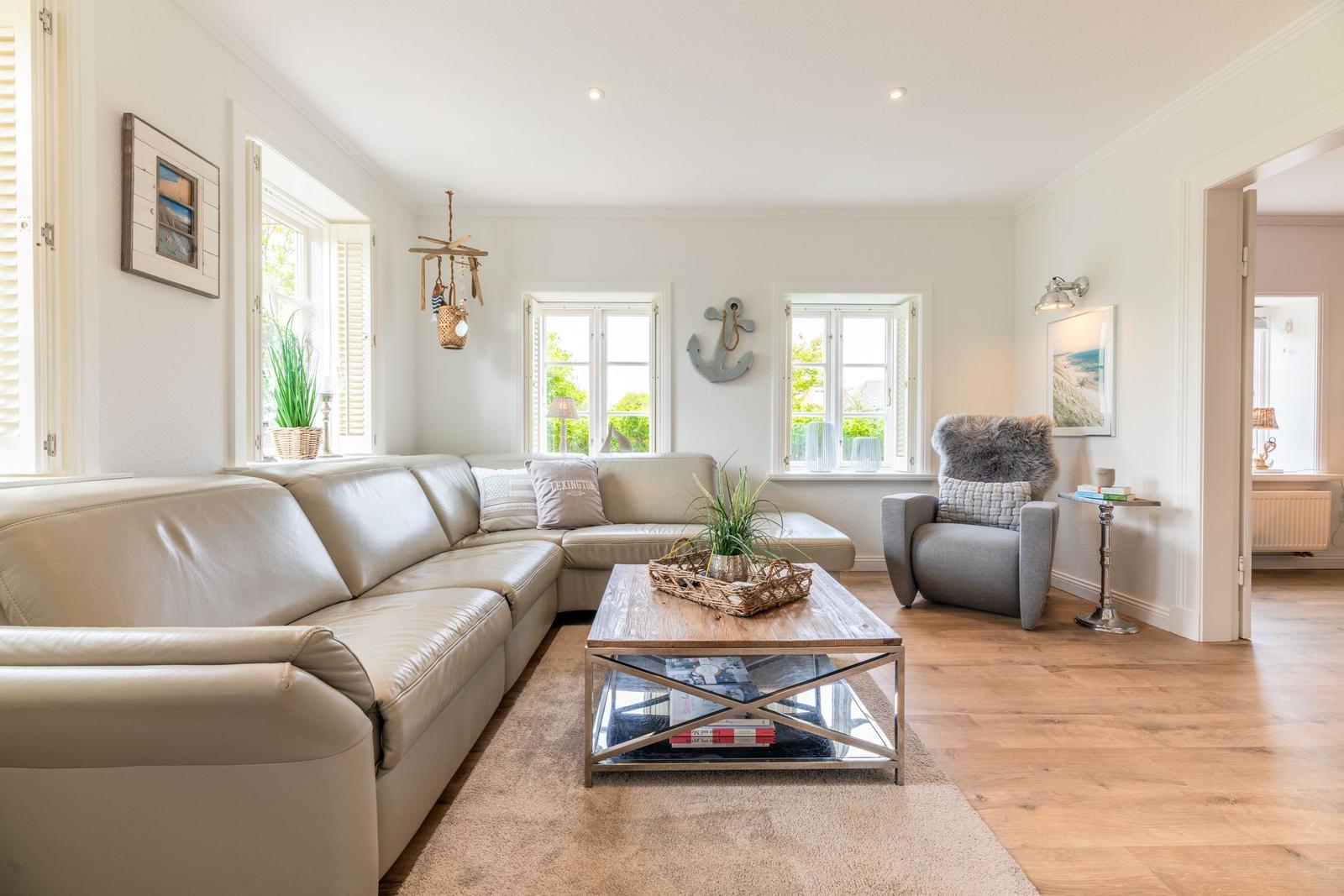 Wohnzimmer mit Sofa, Sessel und Tisch. Fenster mit Jalousien und Wanddekoration.