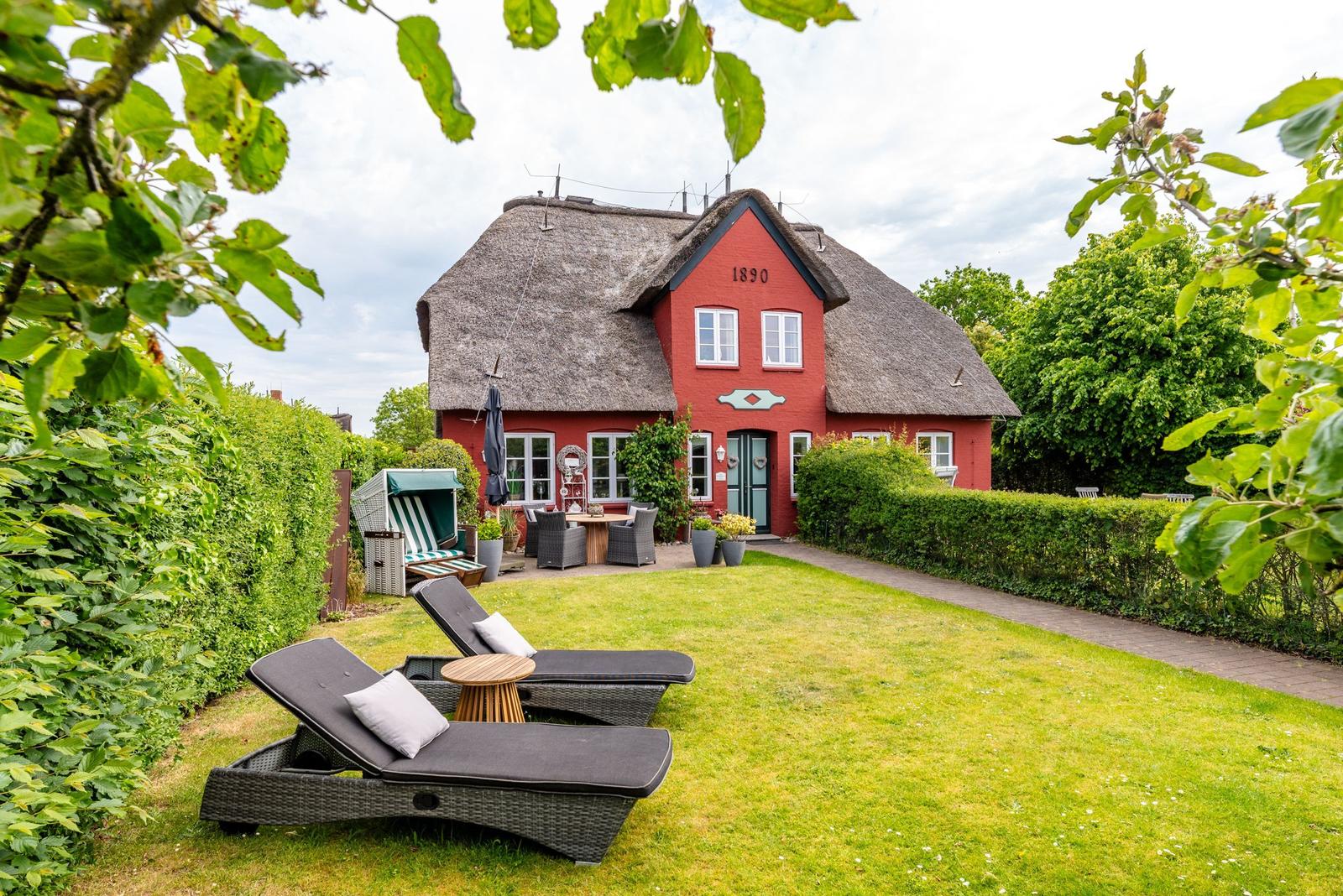 Rotes Haus mit Strohdach und Garten mit Liegen.