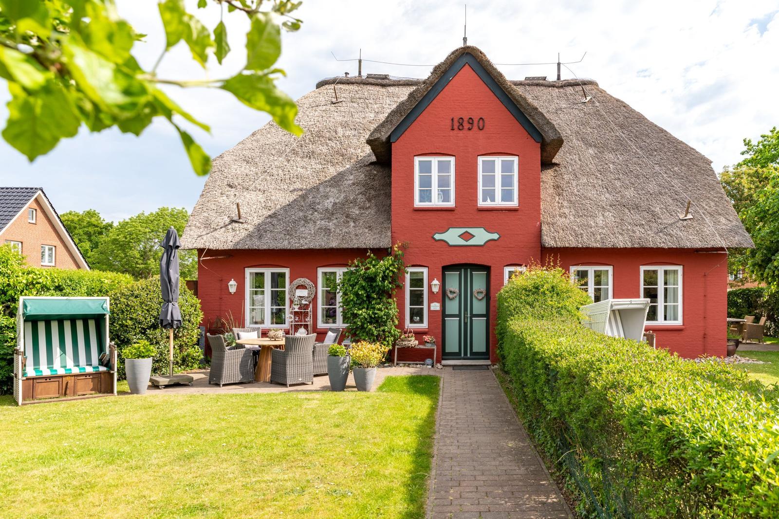 Rotes Haus mit Strohdach, Garten und Terrasse mit Sitzgelegenheiten.