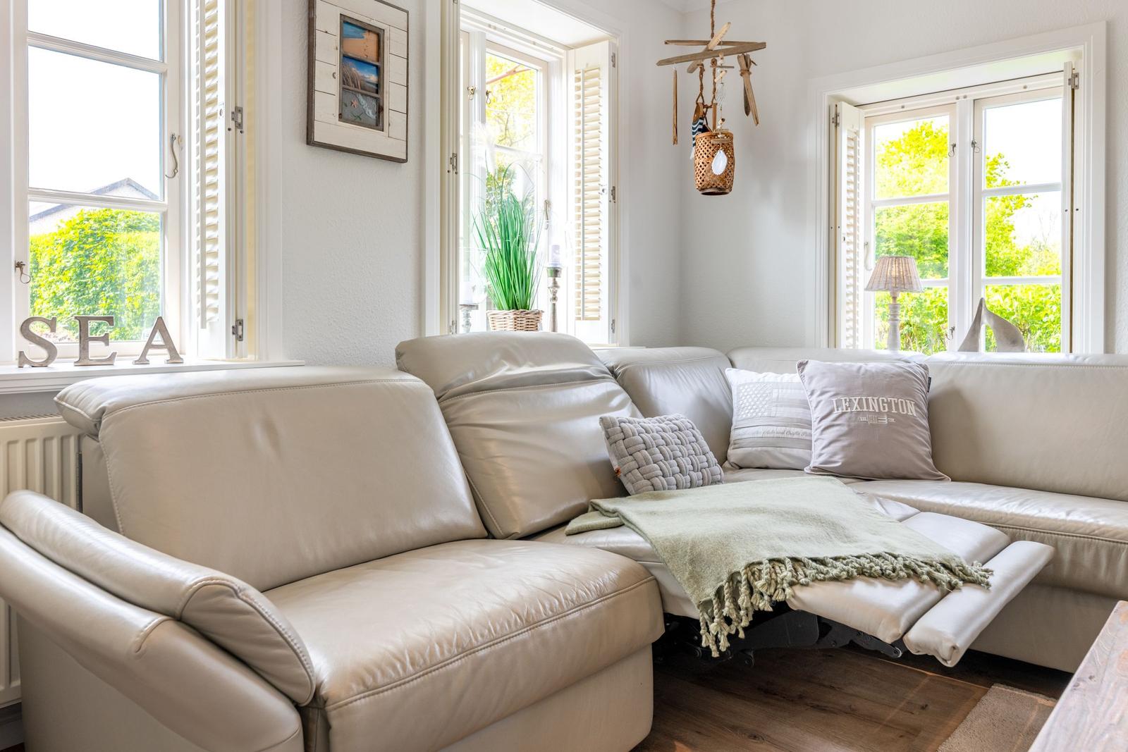 Ein Wohnzimmer mit cremefarbenem Sofa, Fenstern und einem Wandbild.