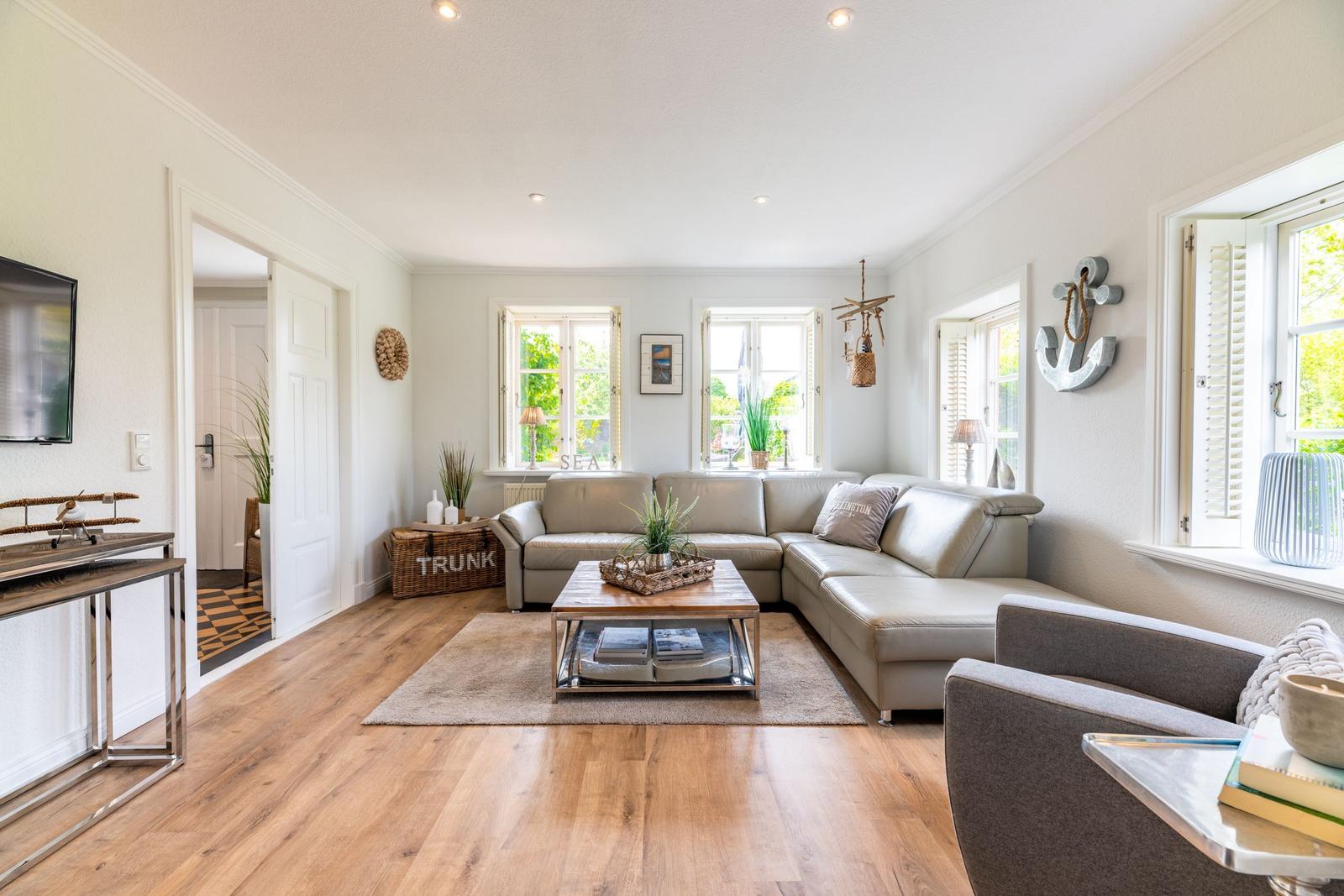 Wohnzimmer mit Sofa, Couchtisch und Fenstern. Holzboden und Wanddekoration.