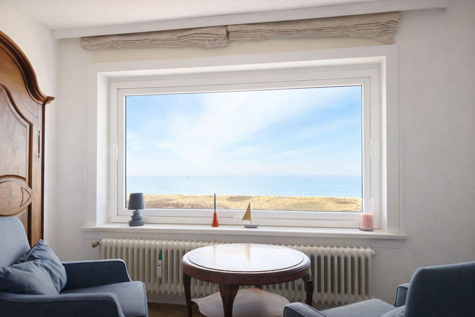 Zimmer mit Blick aufs Meer. Fenster, Tisch, Stühle und Heizkörper sind sichtbar.