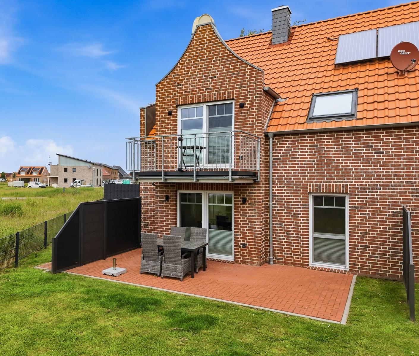 Zweistöckiges Haus mit Balkon, Terrasse und Garten. Solaranlage auf Dach.