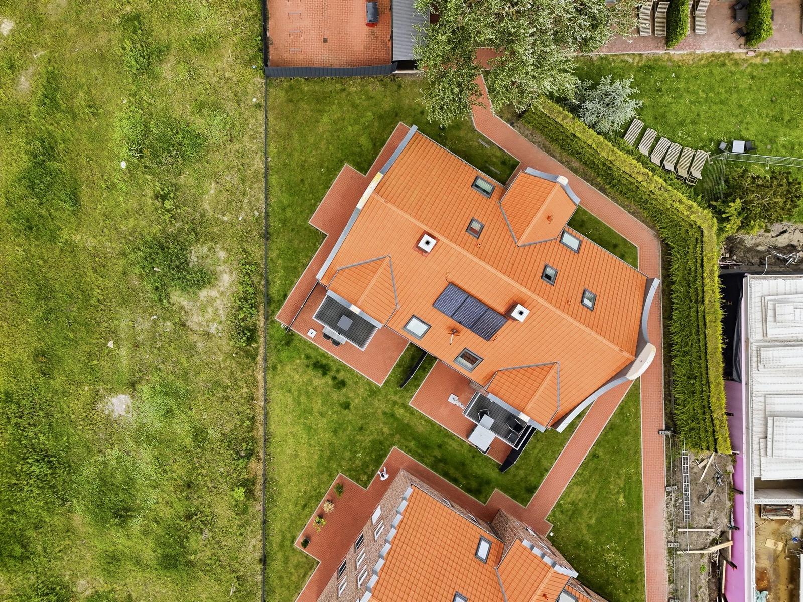 Haus mit orangefarbenem Dach, Garten und Terrasse mit Sonnenkollektoren.