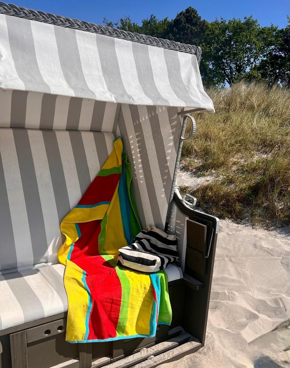 Strandkorb mit buntem Handtuch und Kissen auf Sand