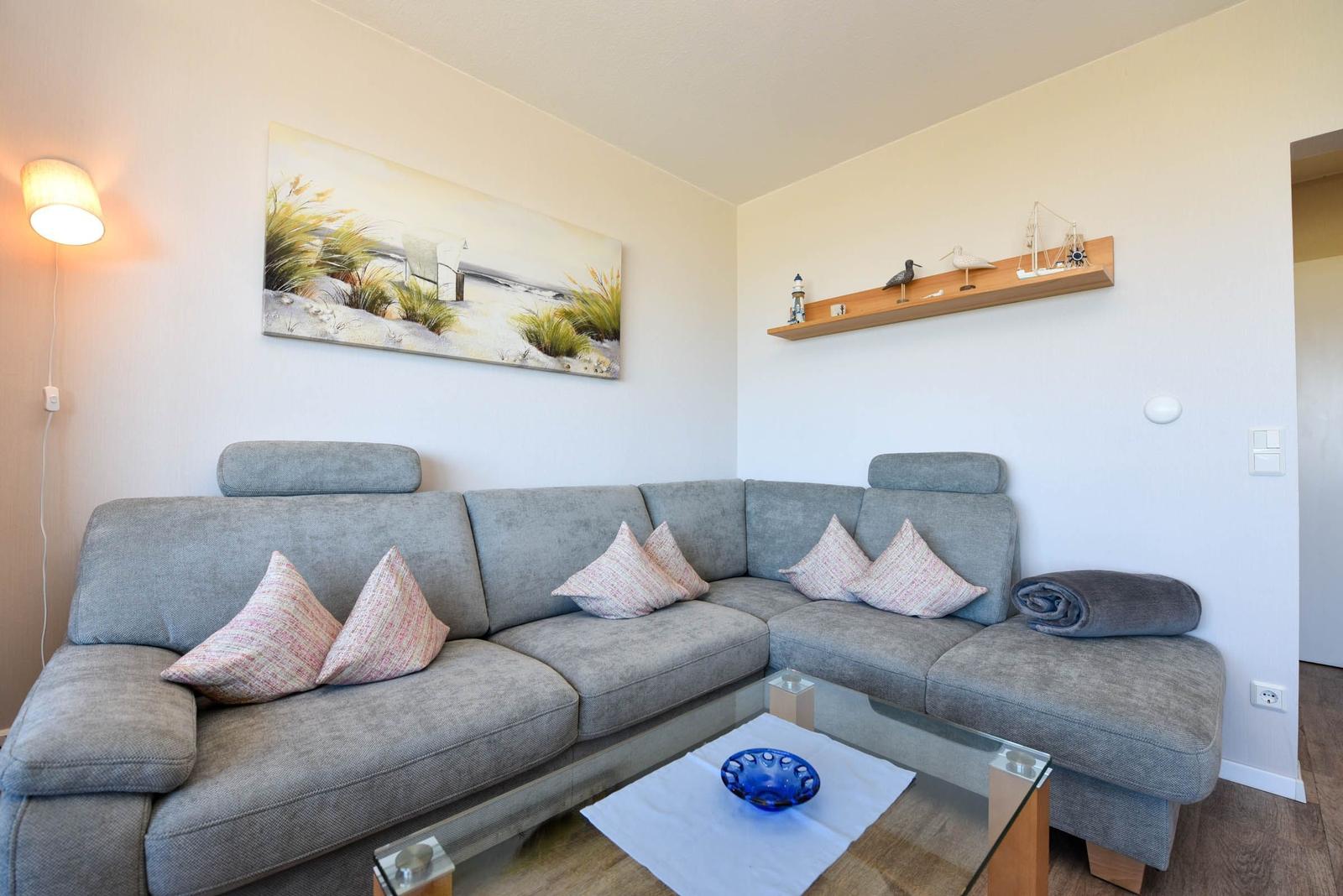 Ein Wohnzimmer mit grauem Sofa, Glas-Tisch und Wandbild.
