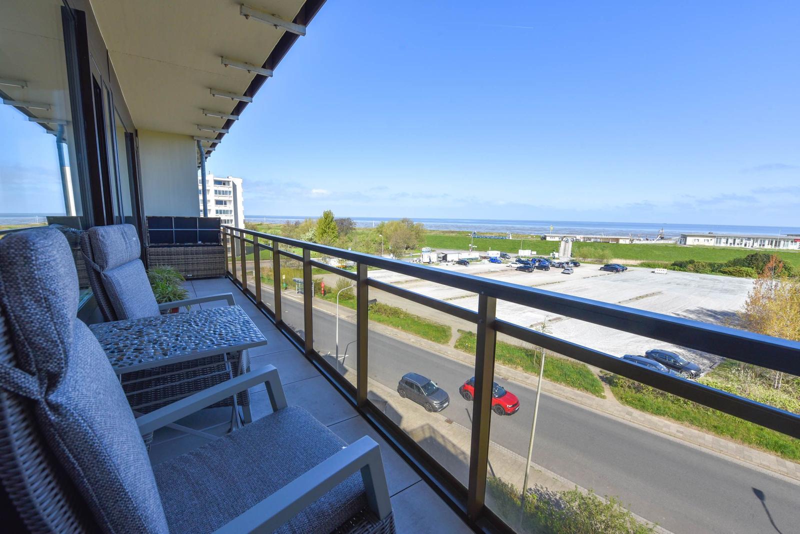 Terrasse mit Sitzgelegenheiten und Blick auf Straße, Parkplatz und Meer.