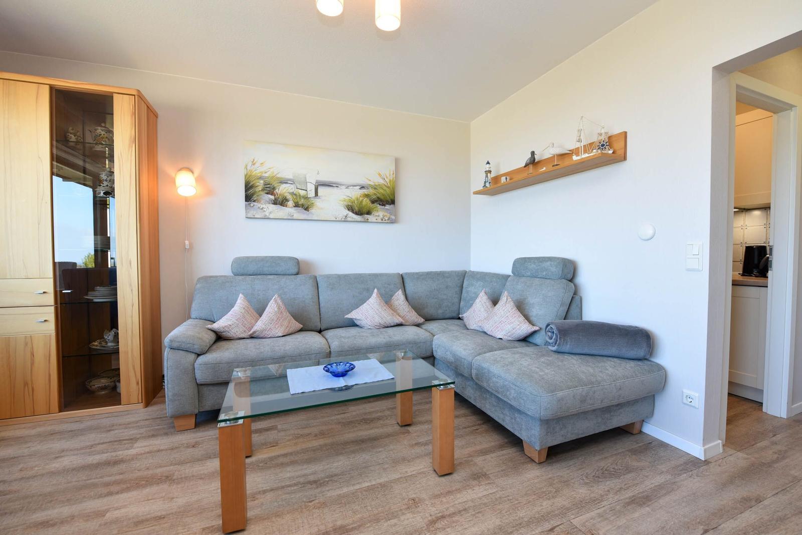 Wohnzimmer mit grauem Sofa, Glas-Tisch und Holzmöbeln. Wandbild und Regal mit Dekoration.