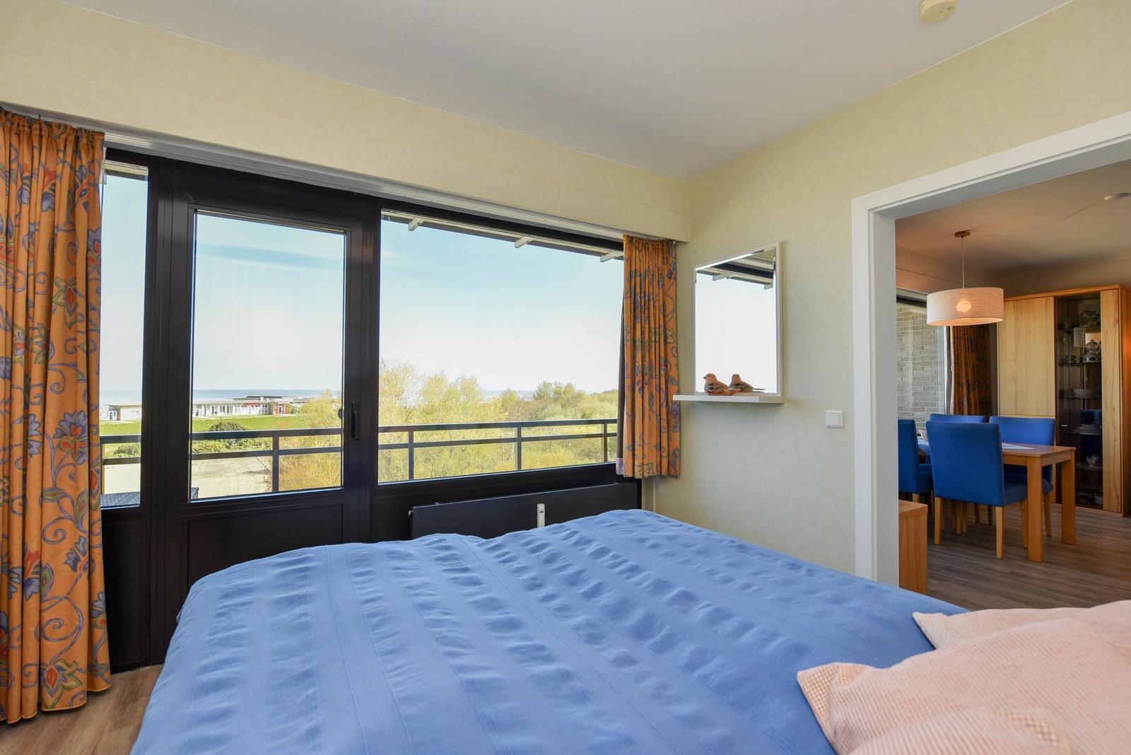 Schlafzimmer mit Blick auf Balkon und Landschaft. Durchgang in Esszimmer mit Tisch und Stühlen.