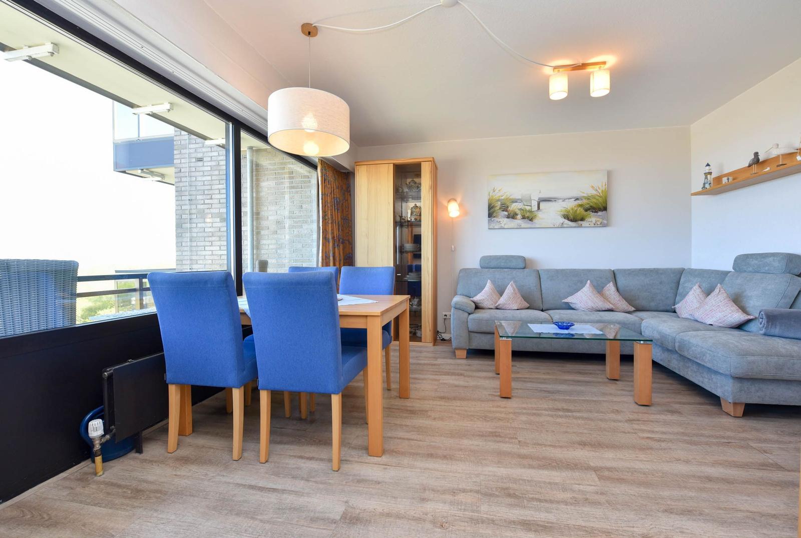 Wohn- und Essbereich mit Sofa, Tisch und Stühlen. Große Fensterfront mit Blick.