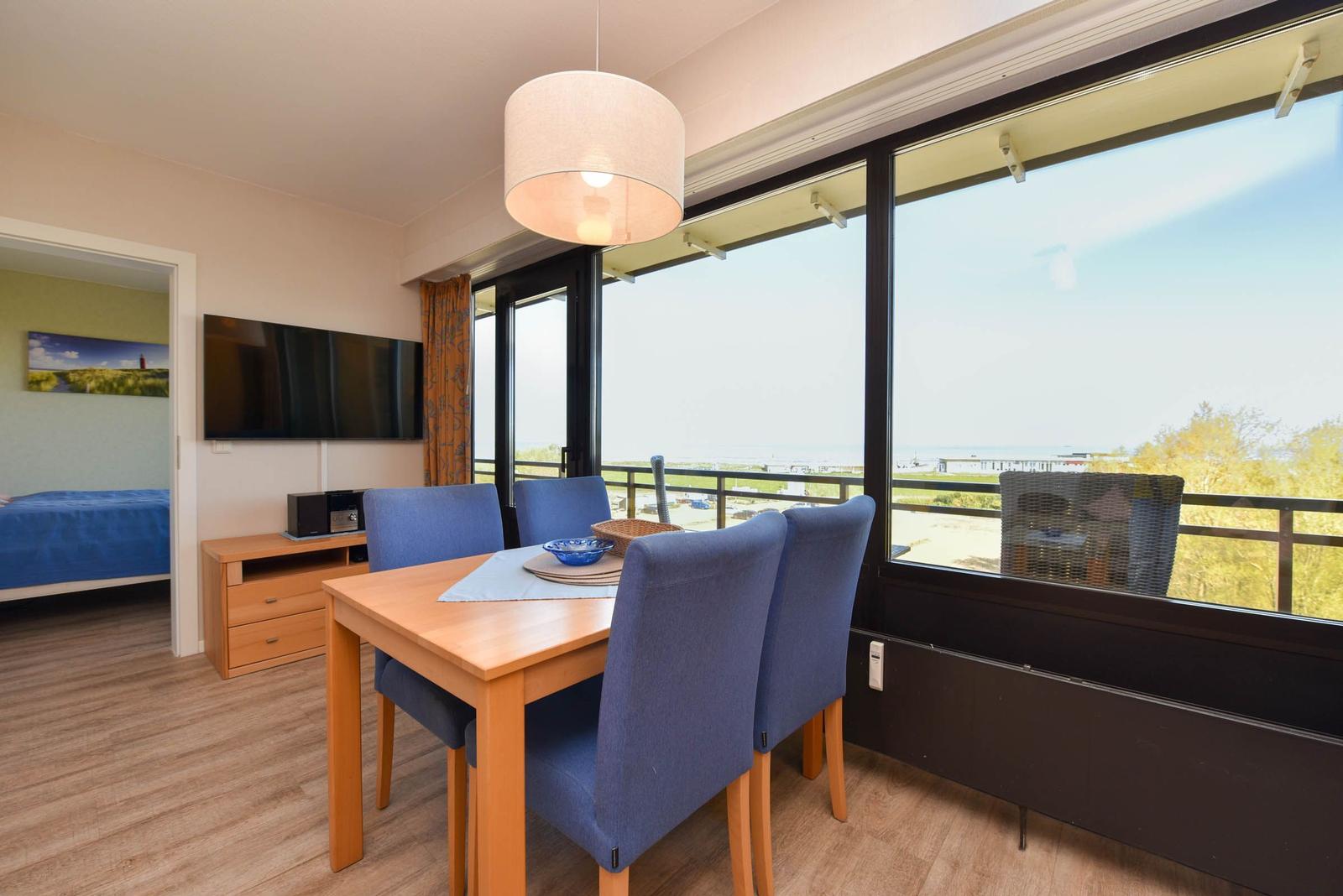 Esszimmer mit Tisch, Stühlen und Blick auf Balkon. Fernseher und Schlafzimmer sichtbar.