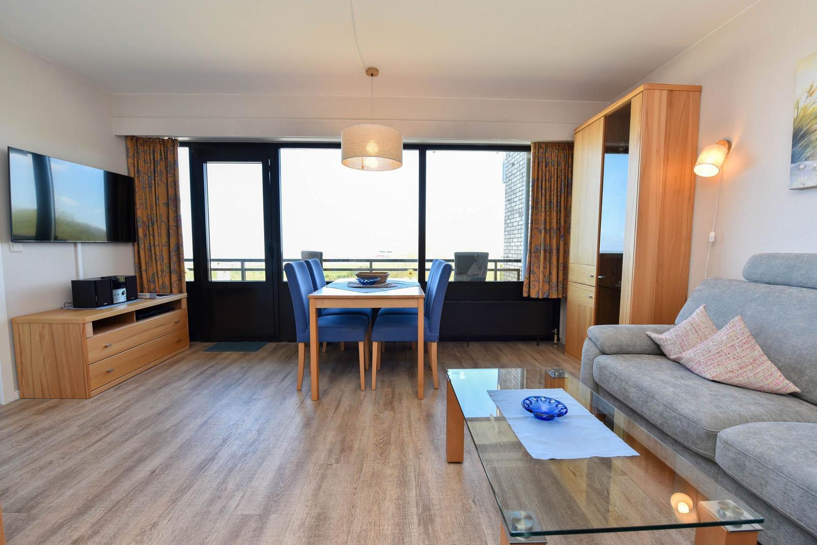 Wohn- und Essbereich mit Sofa, Tisch, TV und Balkonzugang.
