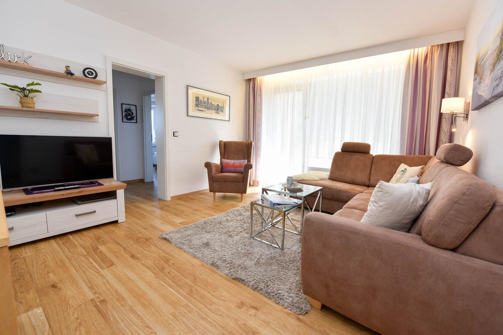 Wohnzimmer mit Sofa, Sessel, Fernseher und Glas-Tisch.