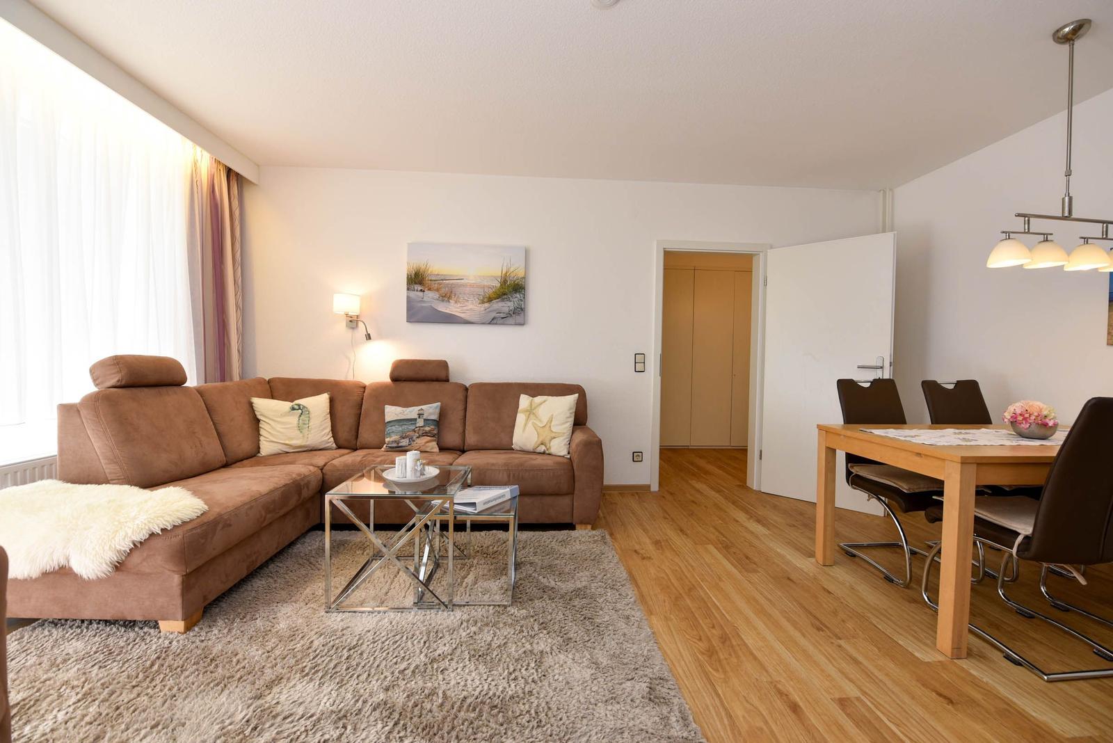 Wohn- und Essbereich mit braunem Sofa, Holzboden und Esstisch mit Stühlen.