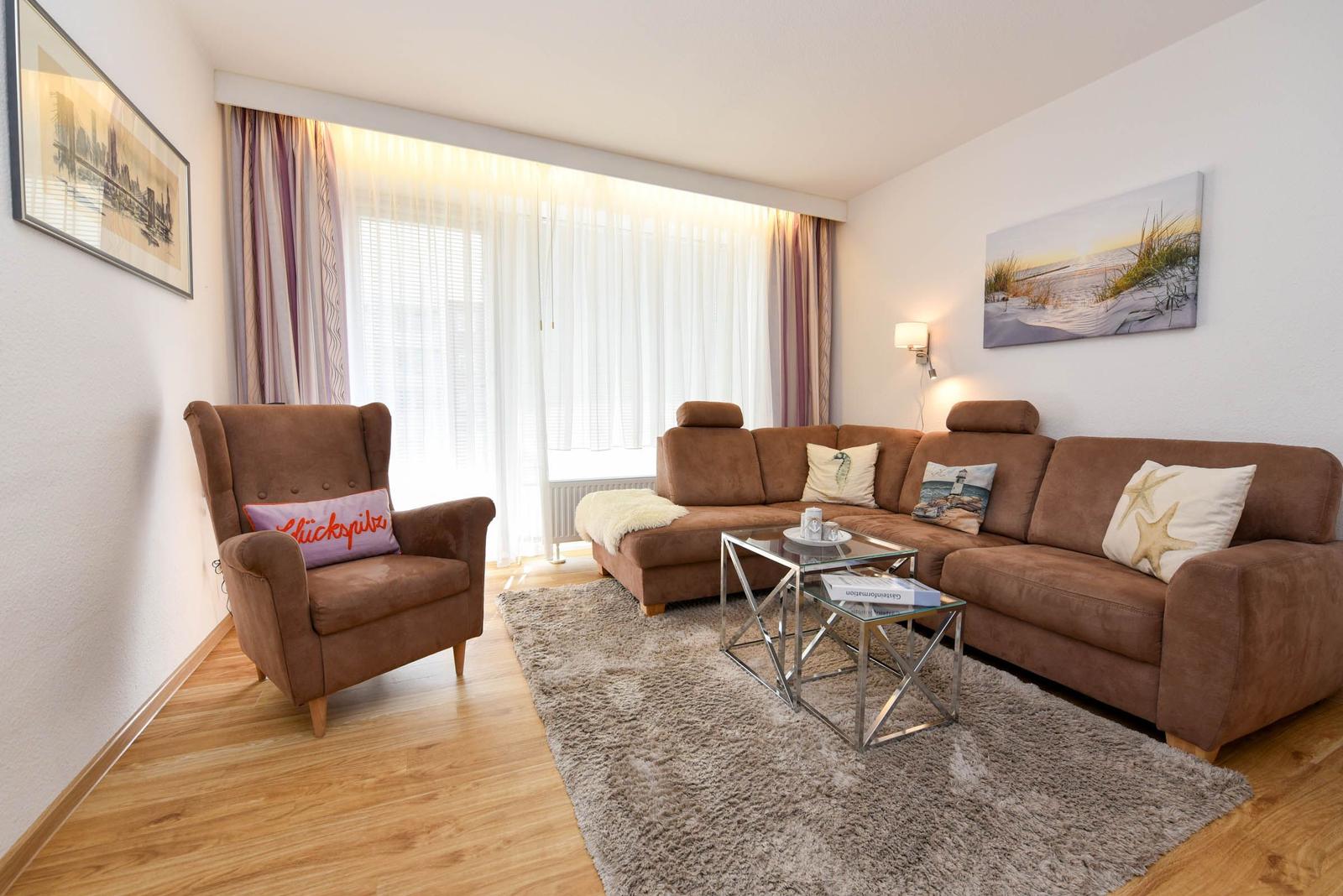 Wohnzimmer mit braunem Sofa, Sessel und Glas-Tisch auf Teppich.