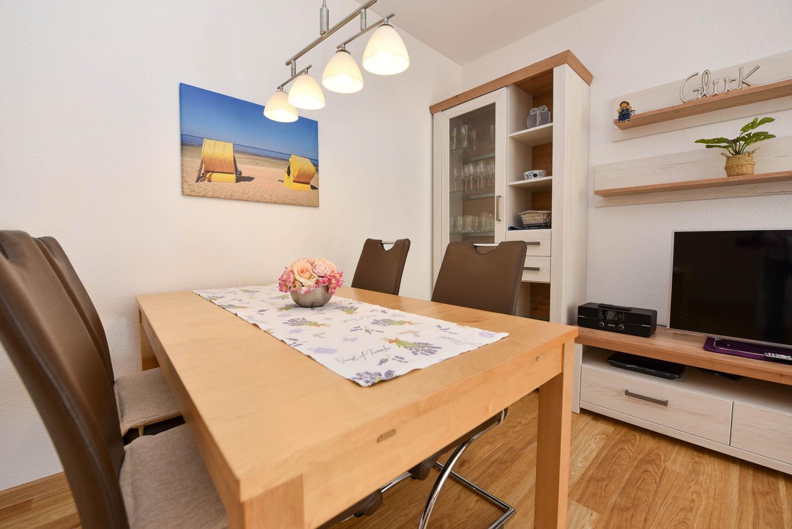 Esstisch mit Stühlen, Wandbild, TV und Schrank im Wohnbereich.