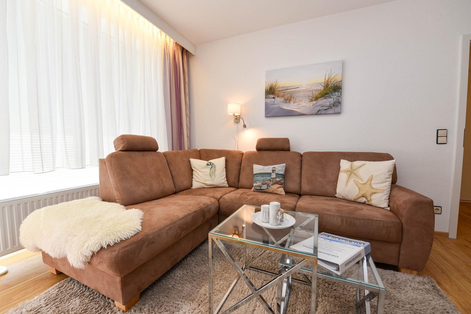 Ein Wohnzimmer mit braunem Sofa, Glas-Tisch und Wandbild mit Strandmotiv.