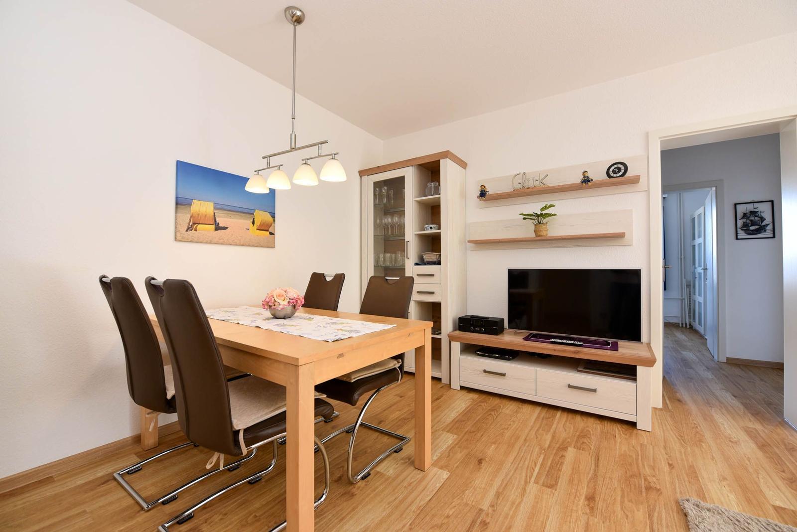 Esszimmer mit Tisch, Stühlen und Fernseher. Holzboden und Wandregale.