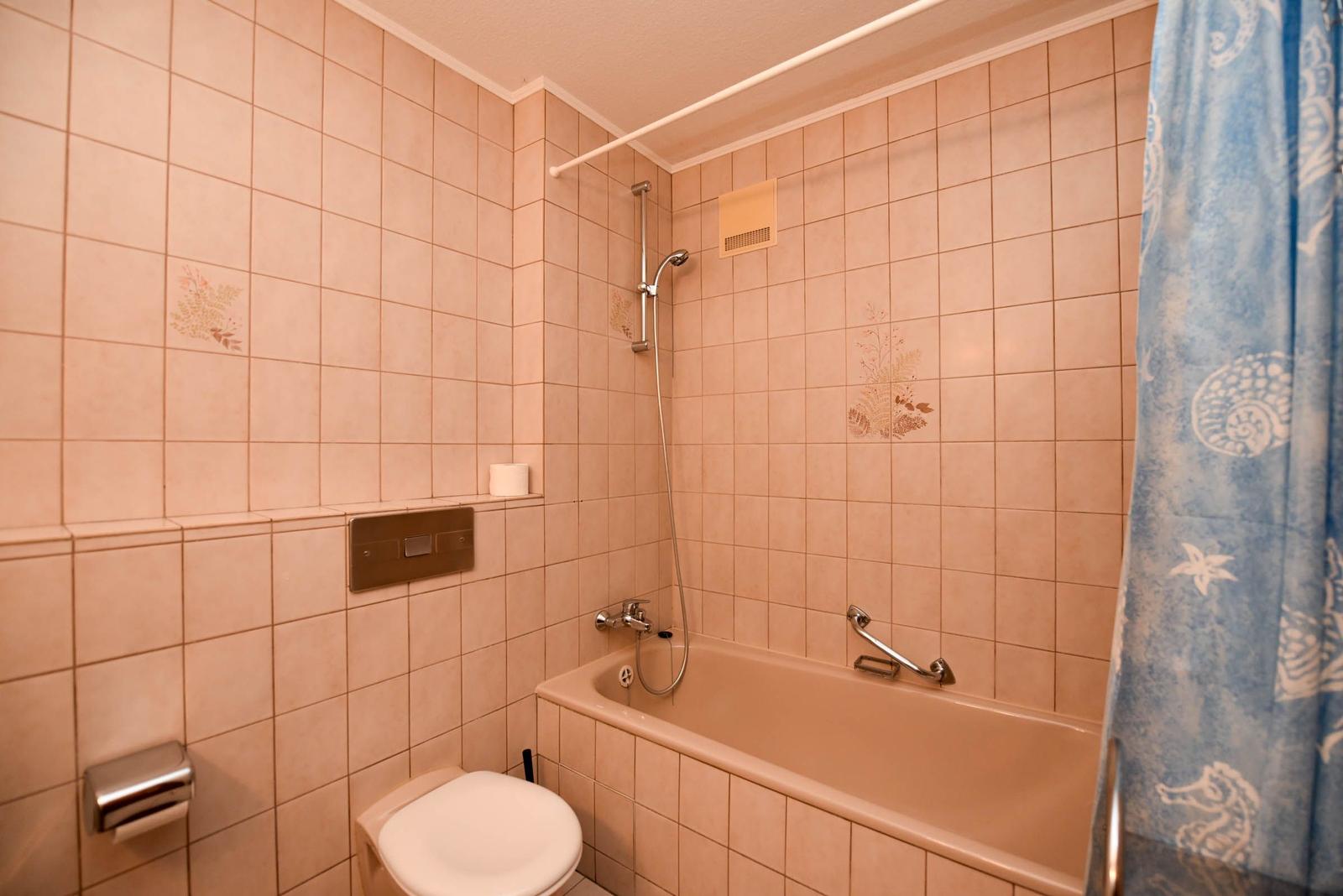 Bad mit Badewanne, Dusche, WC und blauem Vorhang mit Meerestiermotiven.