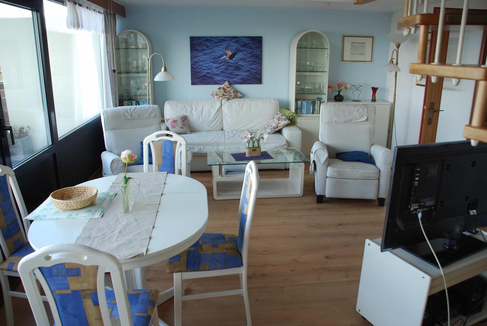 Wohn- und Essbereich mit Sofa, Stühlen und Glaswand. Holzboden und Wandbild sichtbar.
